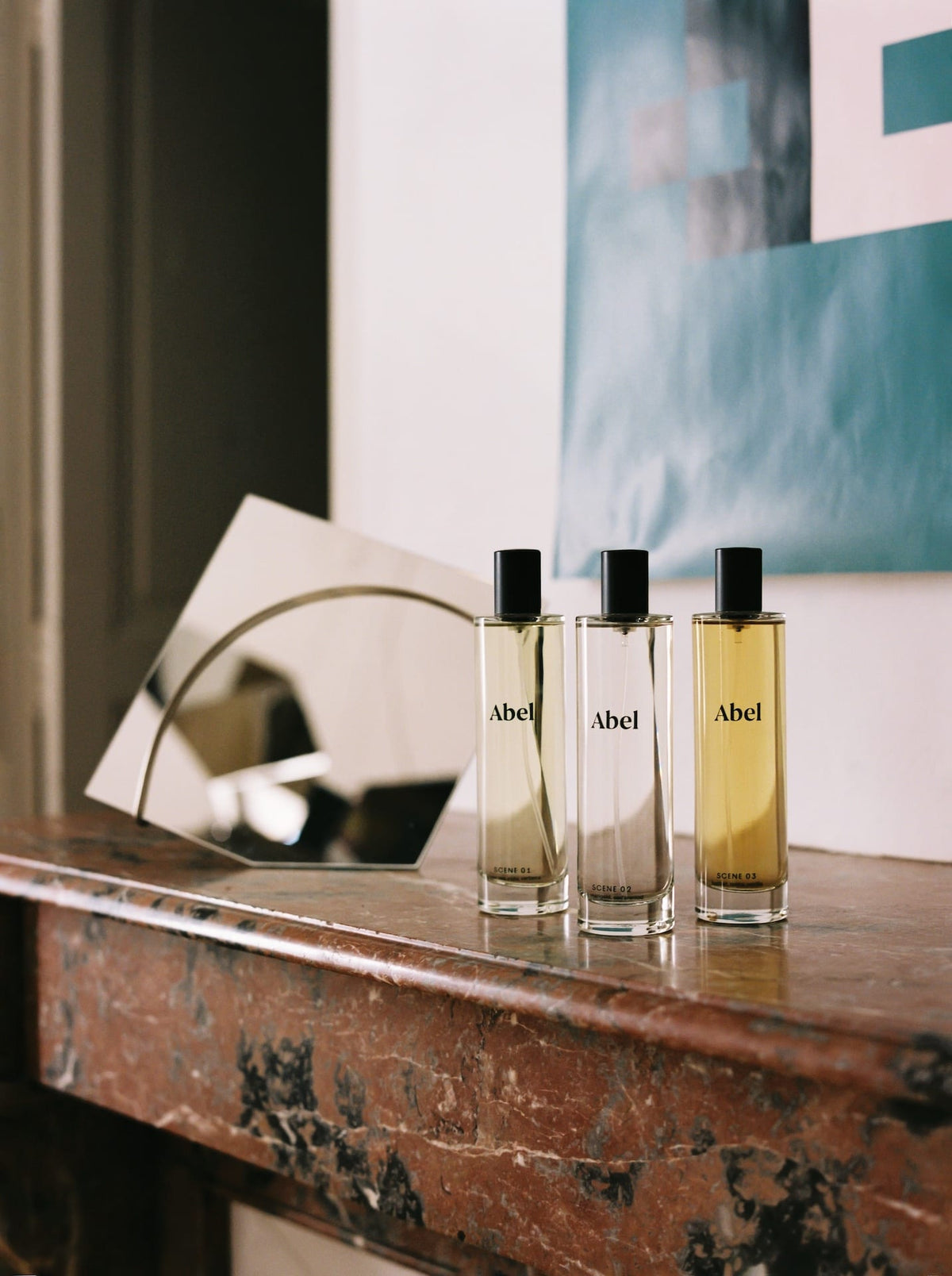 Three bottles of Abel Room Spray – Scene 03 ⋅ leather, tonka, vanilla crafted from natural ingredients on a wooden mantelpiece with a round mirror in the background.