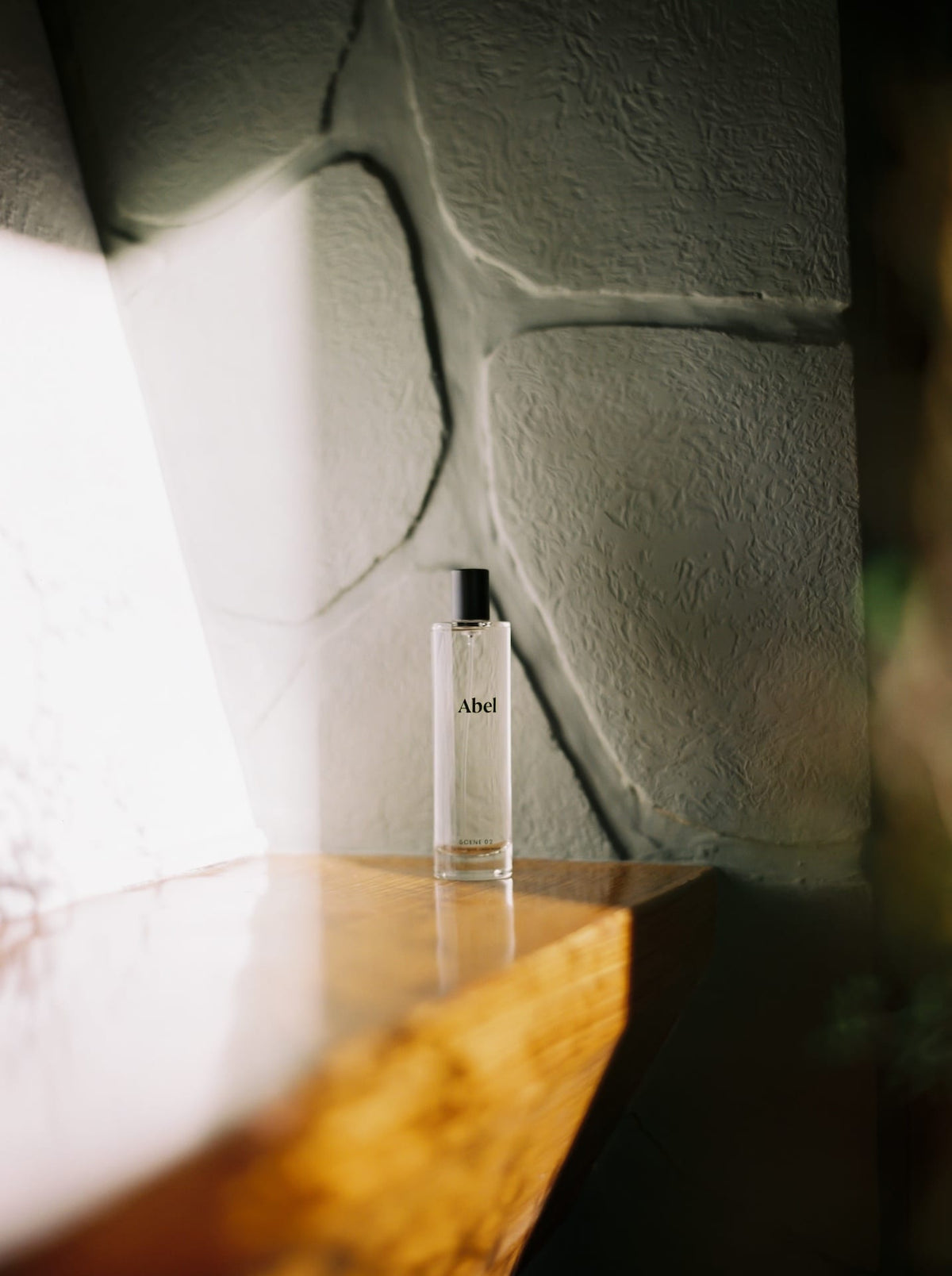 Clear Abel Room Spray bottle on wooden surface with textured wall background and soft lighting.