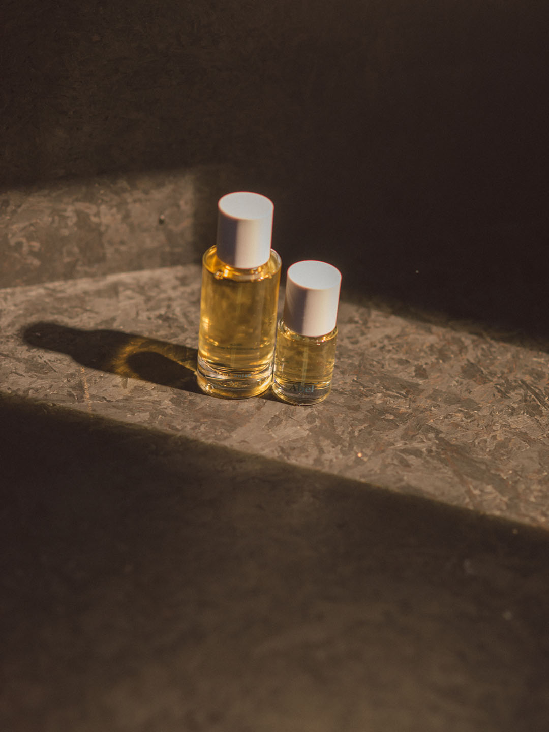 Two vibrant bottles of Abel essential oil, one infused with the smoky amber Black Anise and the other with dynamic star anise, sitting on a table.