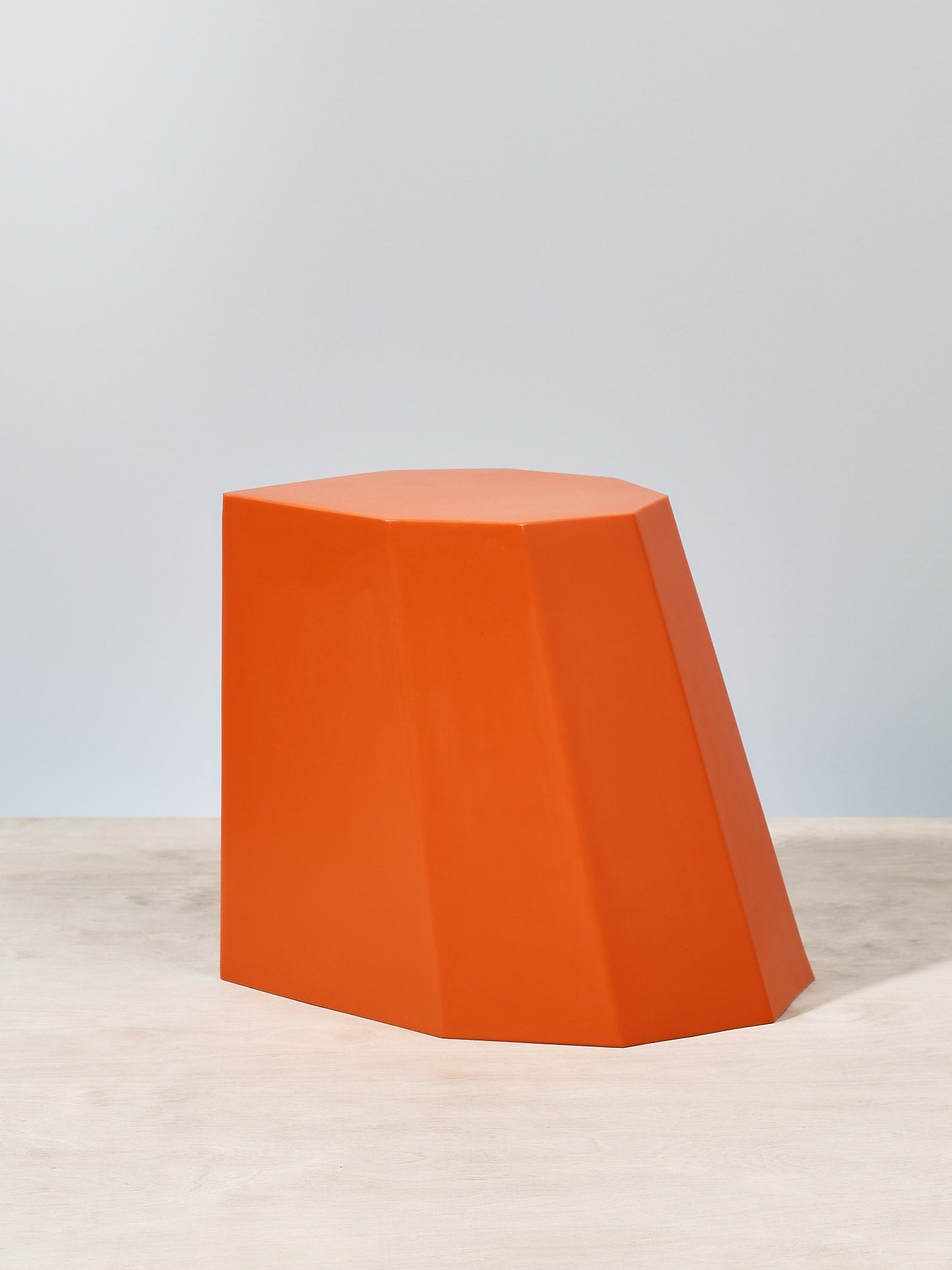 An Arnoldino stool – orange, made by Martino Gamper, sitting on top of a wooden table.