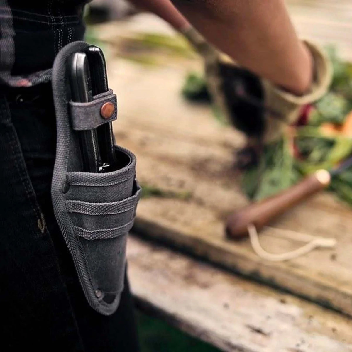 A gardener is holding a Barebones pruner with sheath in a leather holster.