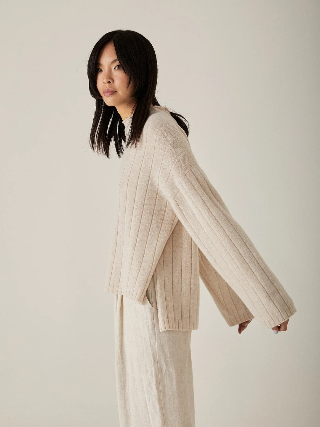 The model is wearing an oversized Echo Knit – Creme sweater and white pants, both crafted from Italian air-spun merino by Francie.
