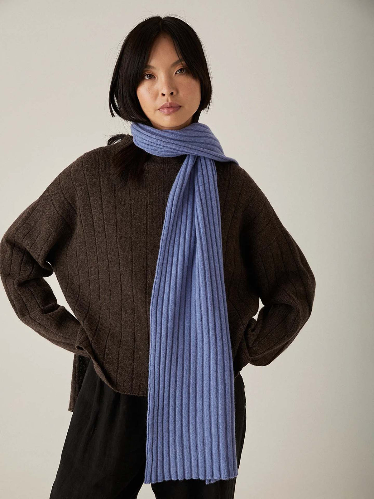 The model is wearing a blue ribbed scarf crafted from Italian air-spun merino by Francie&#39;s Echo Knit – Truffle.