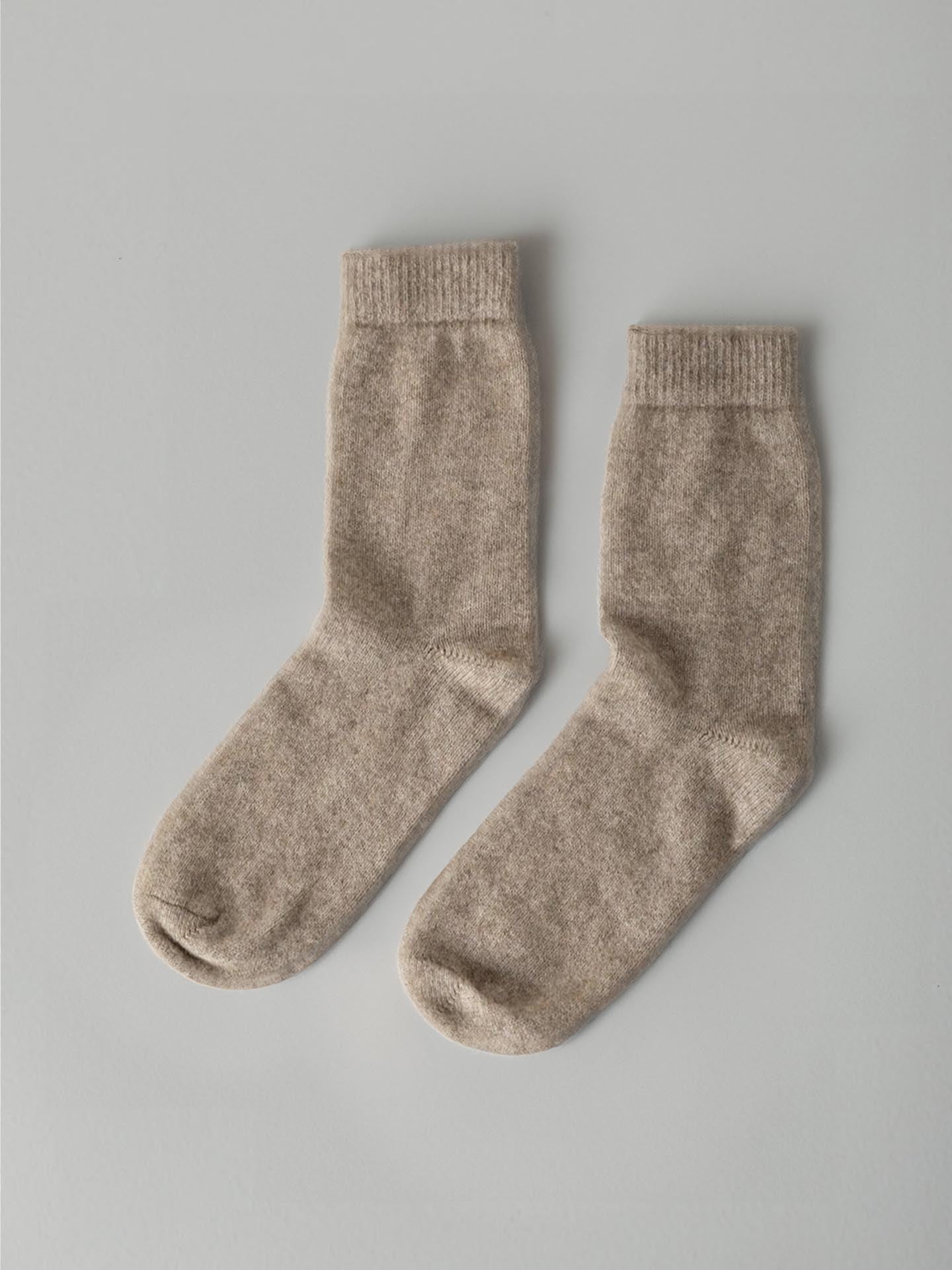 A pair of Possum Merino Socks – Natural from Francie laid flat on a gray surface.