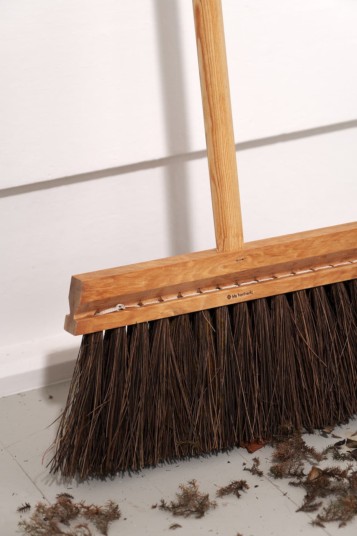 An Outdoor Broom – Birch &amp; Bassine by Iris Hantverk with a wooden handle sitting on the floor.