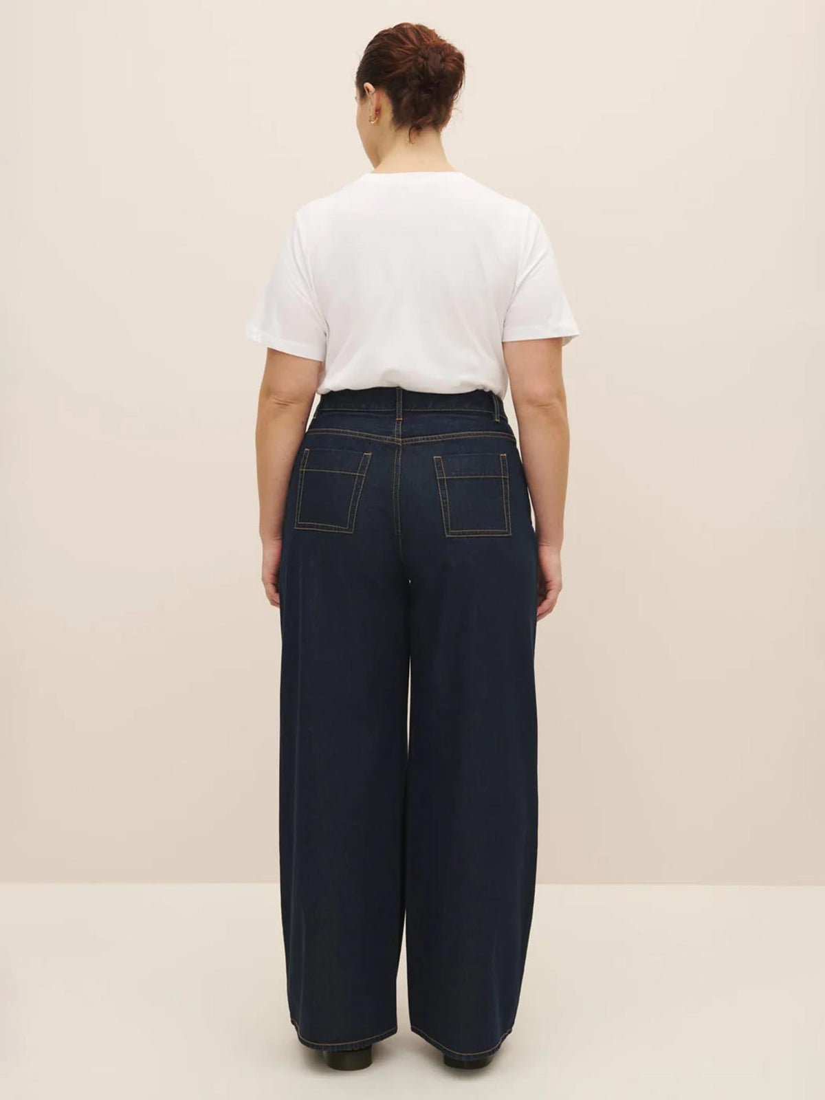 Woman from behind wearing high-waist Kowtow navy trousers and a white t-shirt against a neutral background.