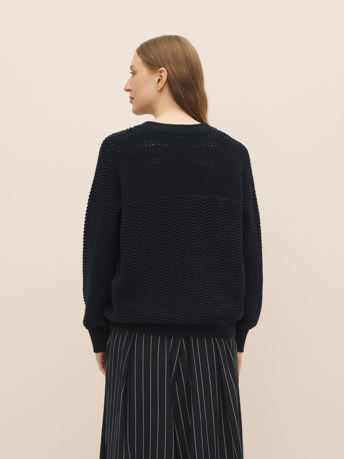 Woman from behind wearing a black rib knit sweater and striped pants against a neutral background, featuring the Zig Zag Crew – Indigo by Kowtow.