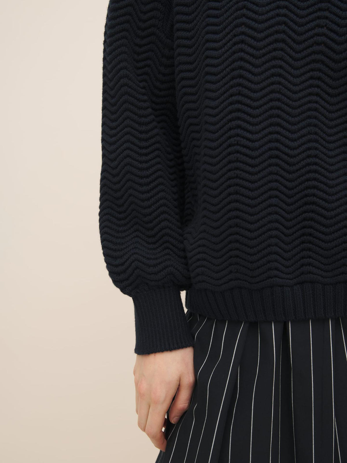 Close-up of a person wearing a Kowtow Zig Zag Crew – Indigo sweater and a black and white striped skirt.