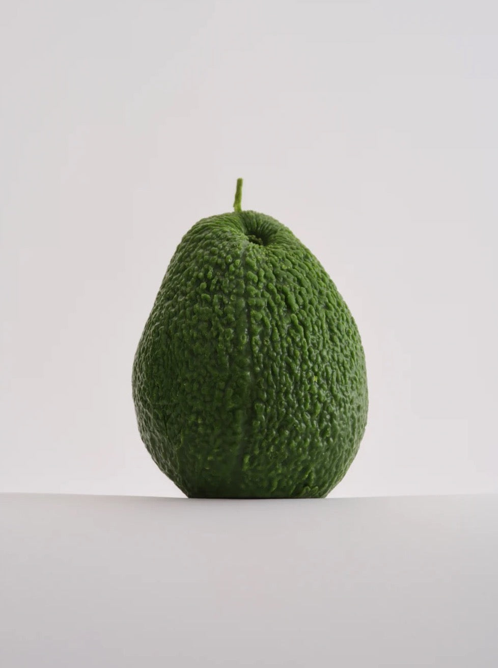 A lifelike Nonna's Grocer Avocado Candle – Large sitting on a white surface.