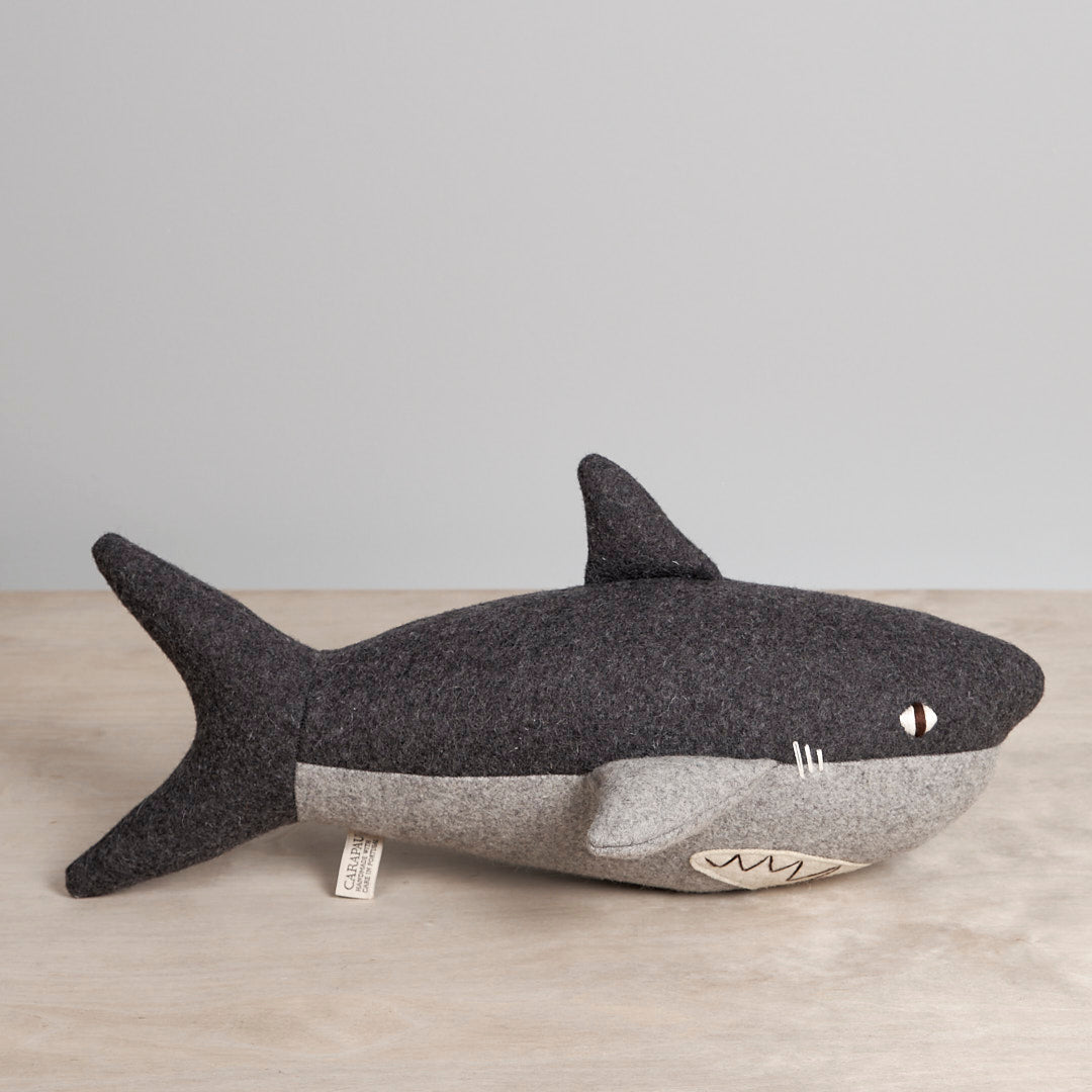 A BEN, the Great White Shark shaped felt toy on a wooden table from the brand Carapau.