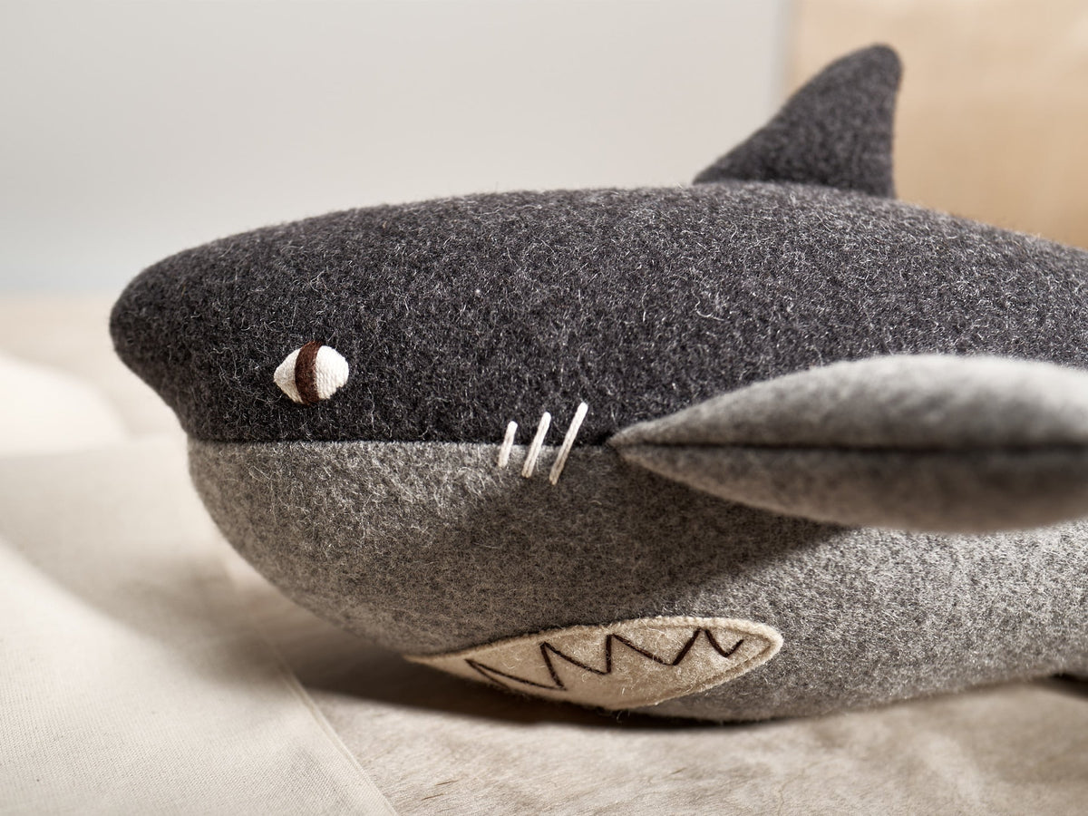 A BEN, the Great White Shark stuffed animal is laying on a bed.