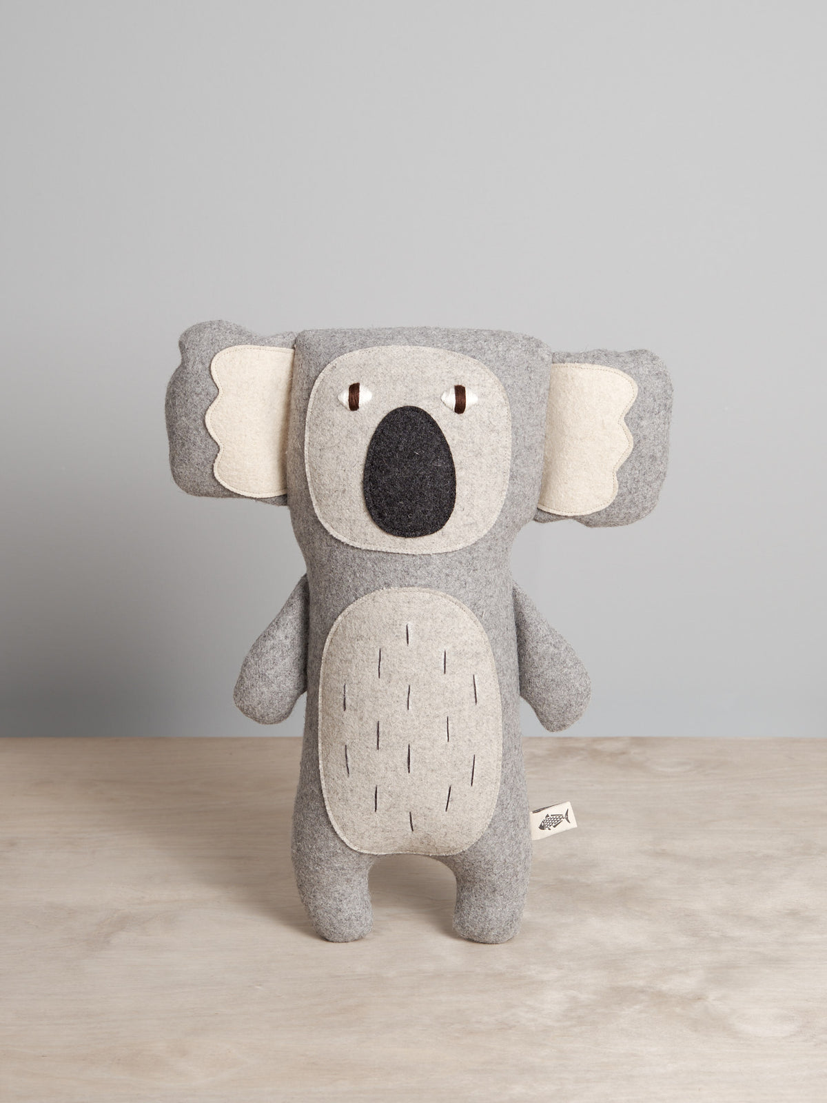 A grey CHARLIE, the Koala stuffed animal on a wooden table. (Brand: Carapau)