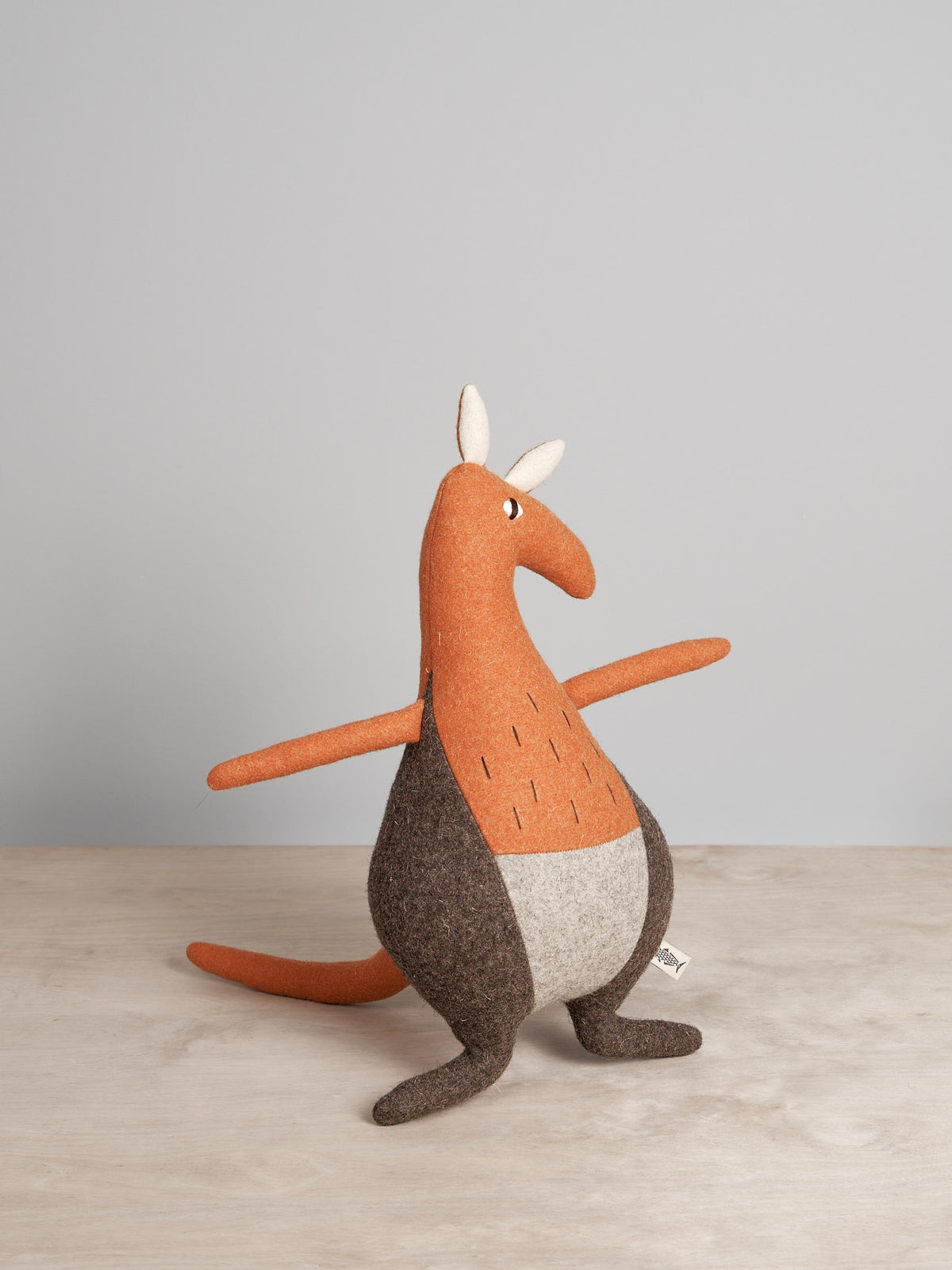 A JOE, the Kangaroo toy is sitting on a wooden table.
