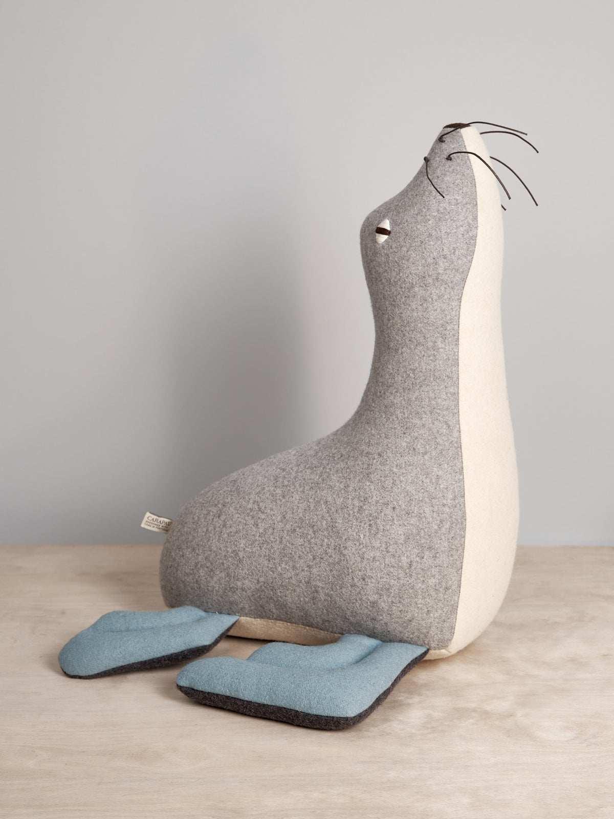 A grey and blue KALI, the Antarctic Fur Seal stuffed animal by Carapau on a table.