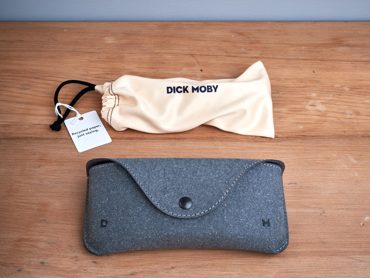A pair of Seattle Sunglasses – Blue Lagoon by Dick Moby and a bag on a wooden table.