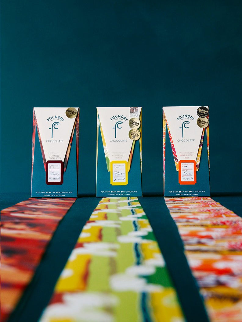 A row of Three Origin Gift Pack - Gold Winners boxes adorned with Foundry Chocolate paper of different colors.