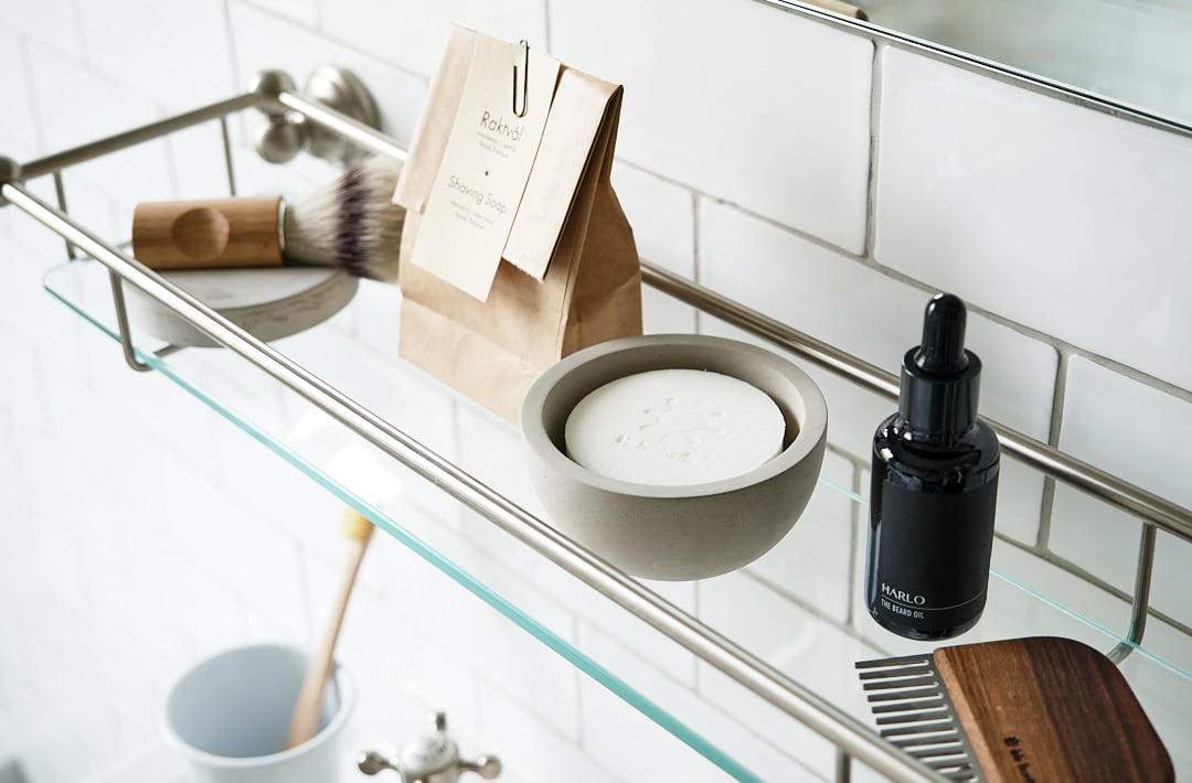 A shelf in a bathroom with a Iris Hantverk beard brush and shaving products including the Shaving Cup with Cedarwood Shaving Soap.