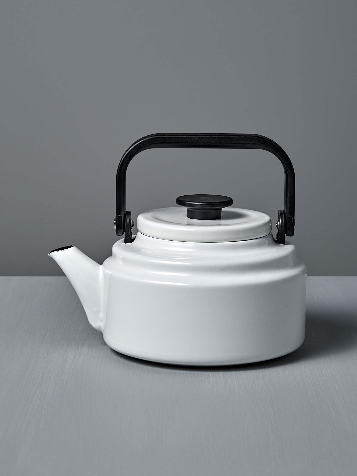 A white Amu Stove-top Kettle with a black handle on a grey background. (Brand: Noda Horo)