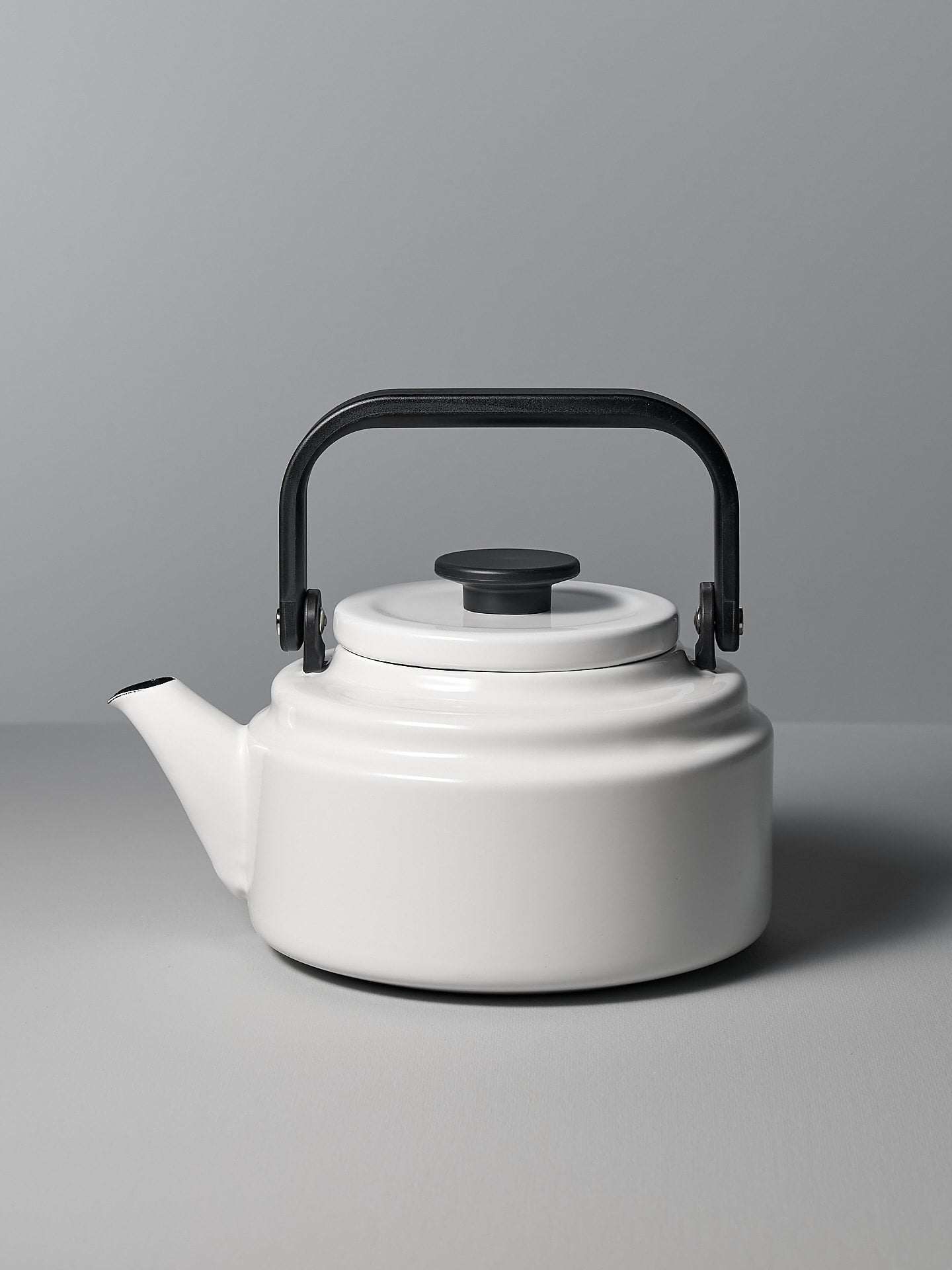 A white Amu Stove-top Kettle with a black handle on a grey background. (Brand: Noda Horo)