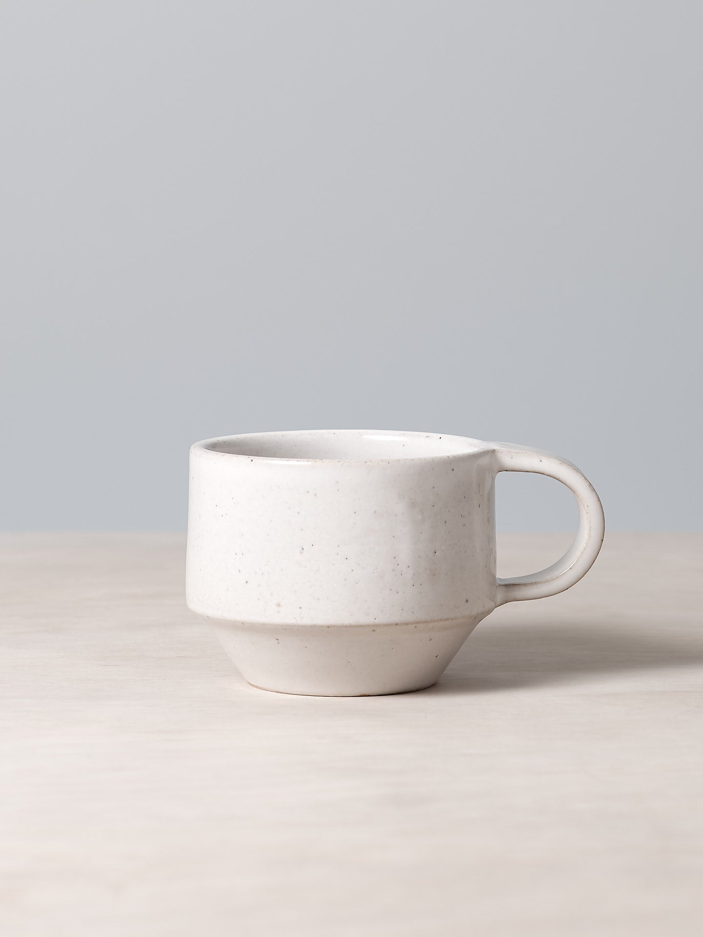 A C-handled Stacking Mug – White by Richard Beauchamp sitting on top of a table.