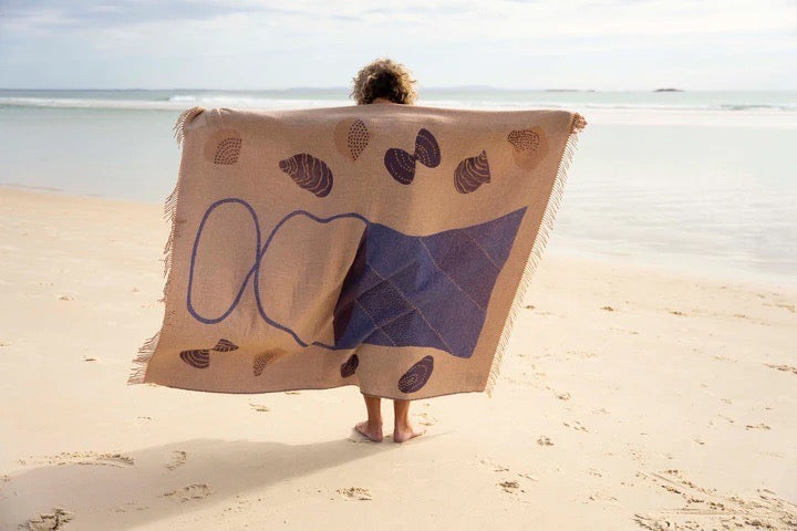A woman holding a Seljak Brand Gather Blanket on the beach.