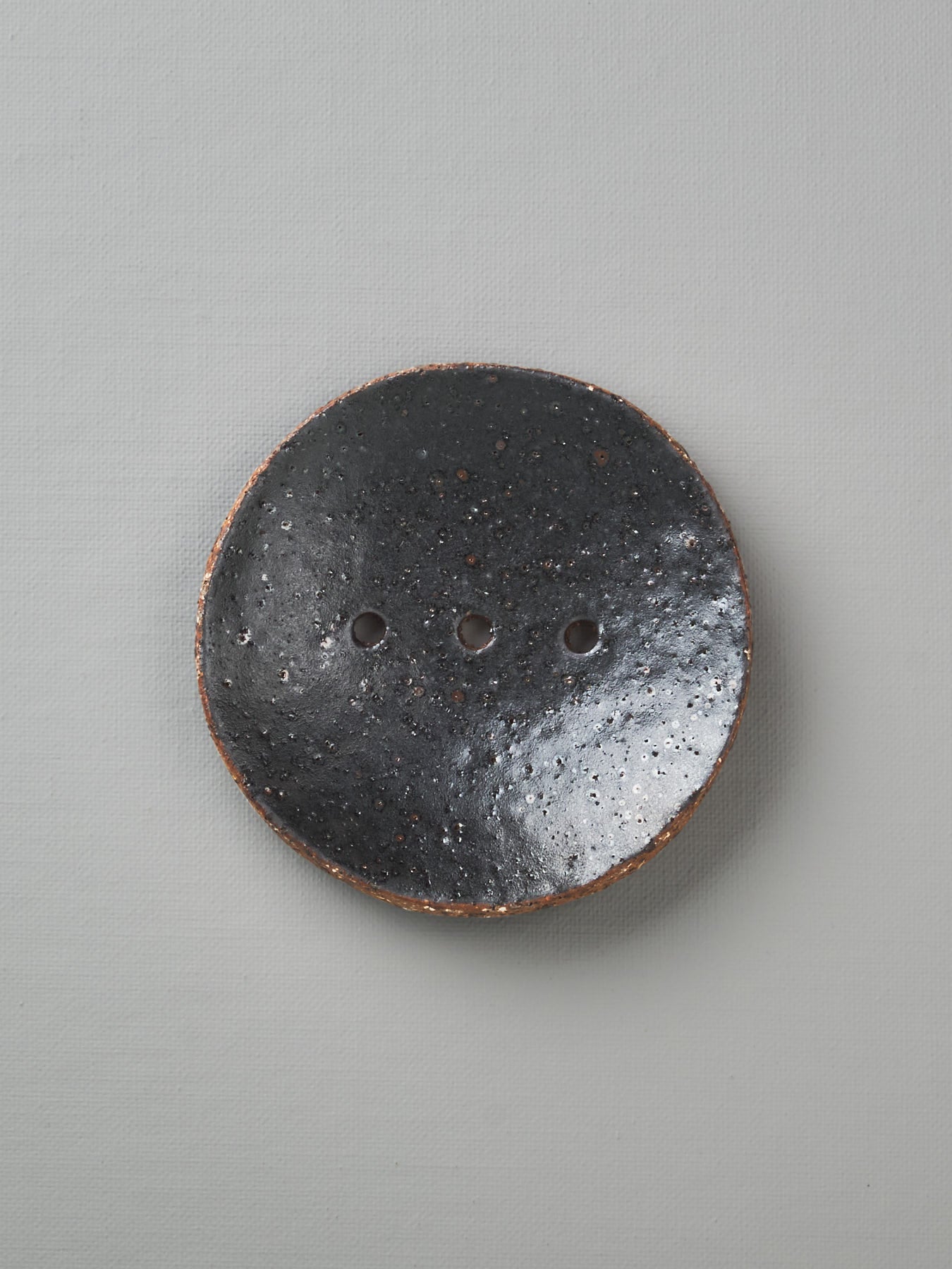 A Round Ceramic Soap Dish - Black with two holes on it.