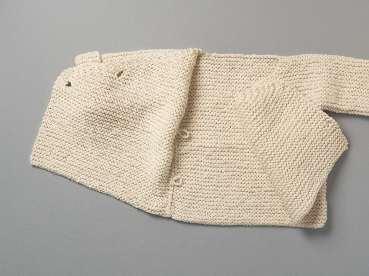 An image of a Hand Knitted Double Breasted Jacket - Natural by Weebits on a grey surface.