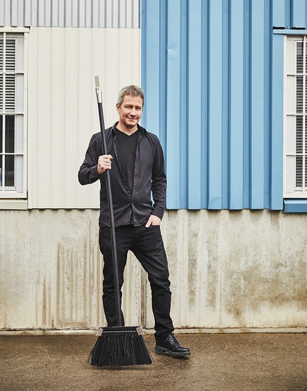 A man holding a broom in front of a building.