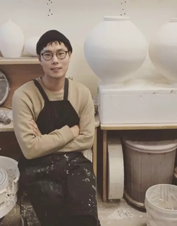 A black and white photo of a man sitting in front of vases.