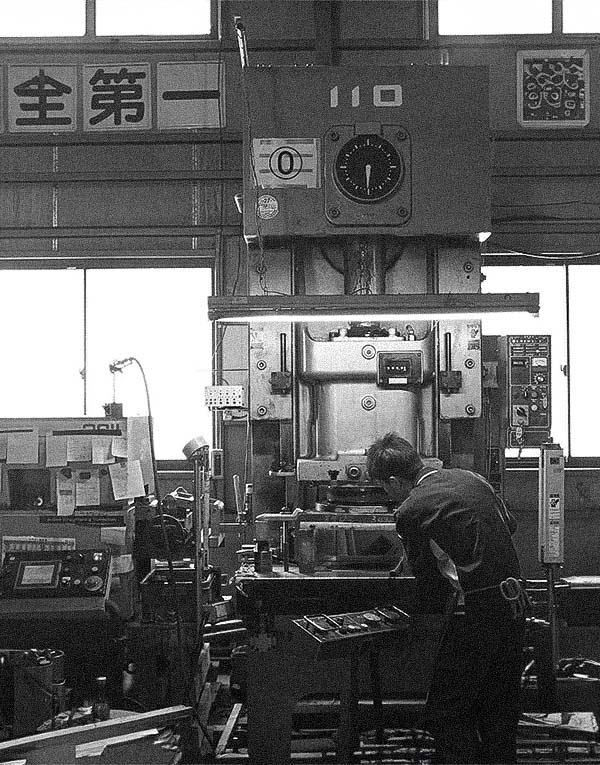 Worker operating an industrial press machine in a manufacturing workshop.