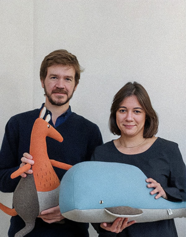 A man holding a kangaroo plush toy and a woman holding a whale plush toy, standing side by side against a plain background.