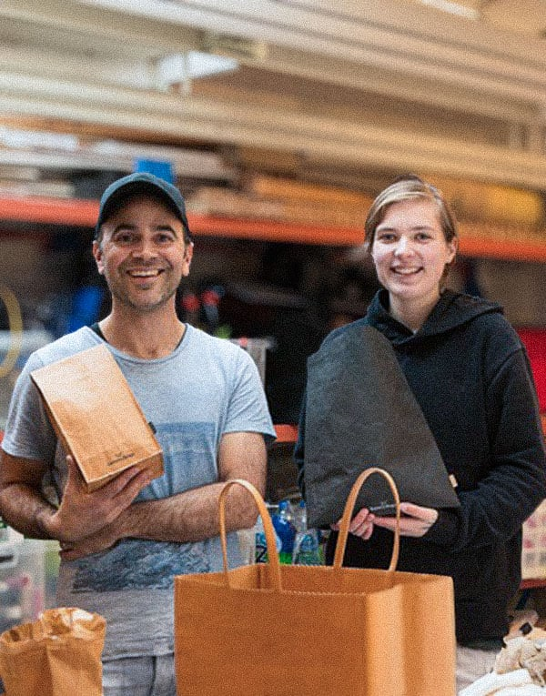 Two people smiling while holding paper shopping bags at a market.