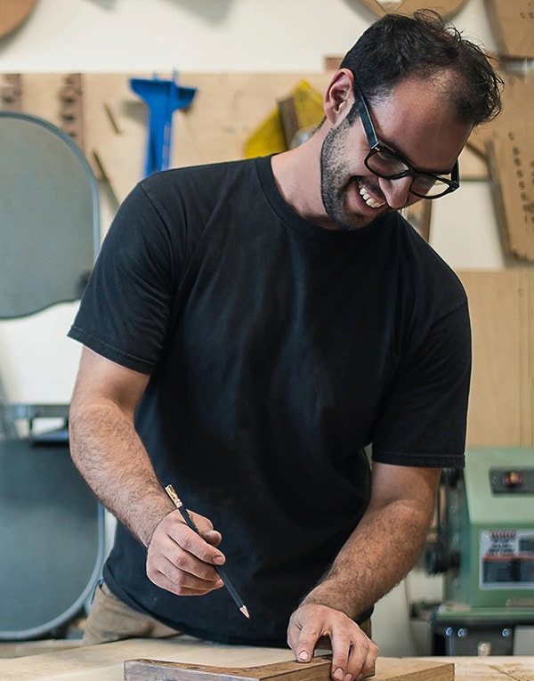 A man in glasses is working on a piece of wood.
