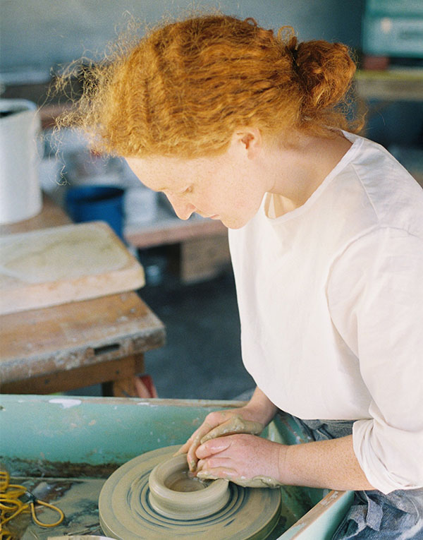 A woman sitting in front of a shelf holding a bowl.