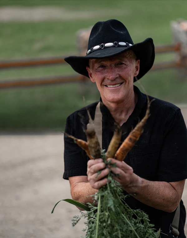 A man in a cowboy hat holding carrots.