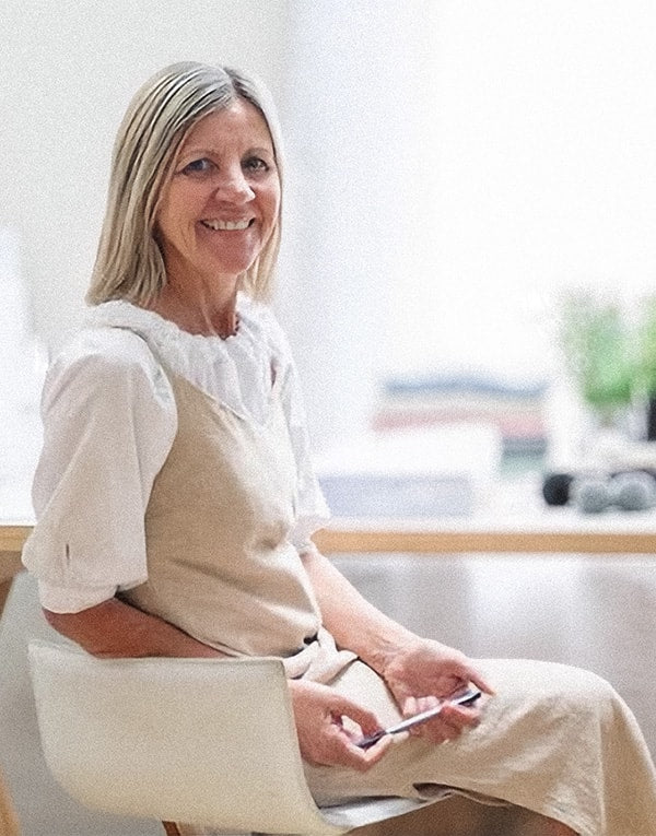 A smiling woman sitting on a chair with a smartphone in her hands.