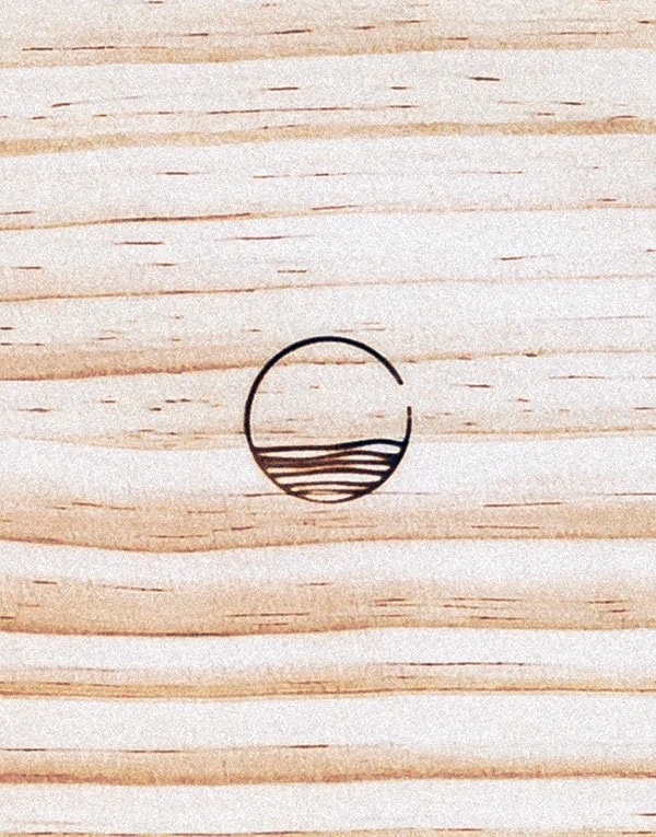 A simple black line illustration of a circle with wavy lines inside, resembling water, is centered on a light wooden surface with visible grain patterns.