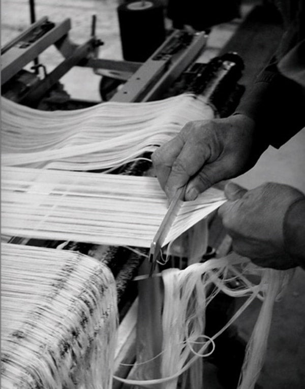 Black and white photo of a man weaving on a loom.