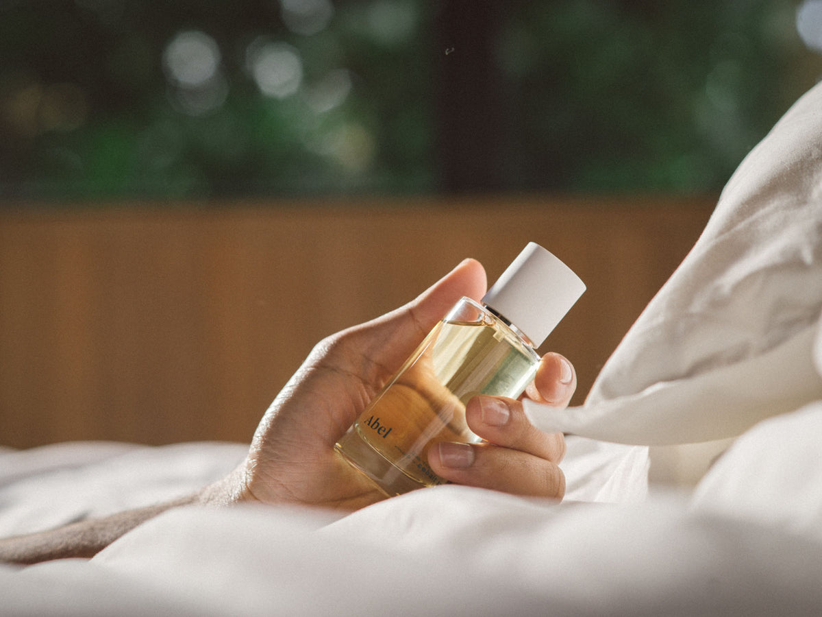 A person holding a bottle of Abel&#39;s Cobalt Amber – a chic, sultry oriental perfume in bed.