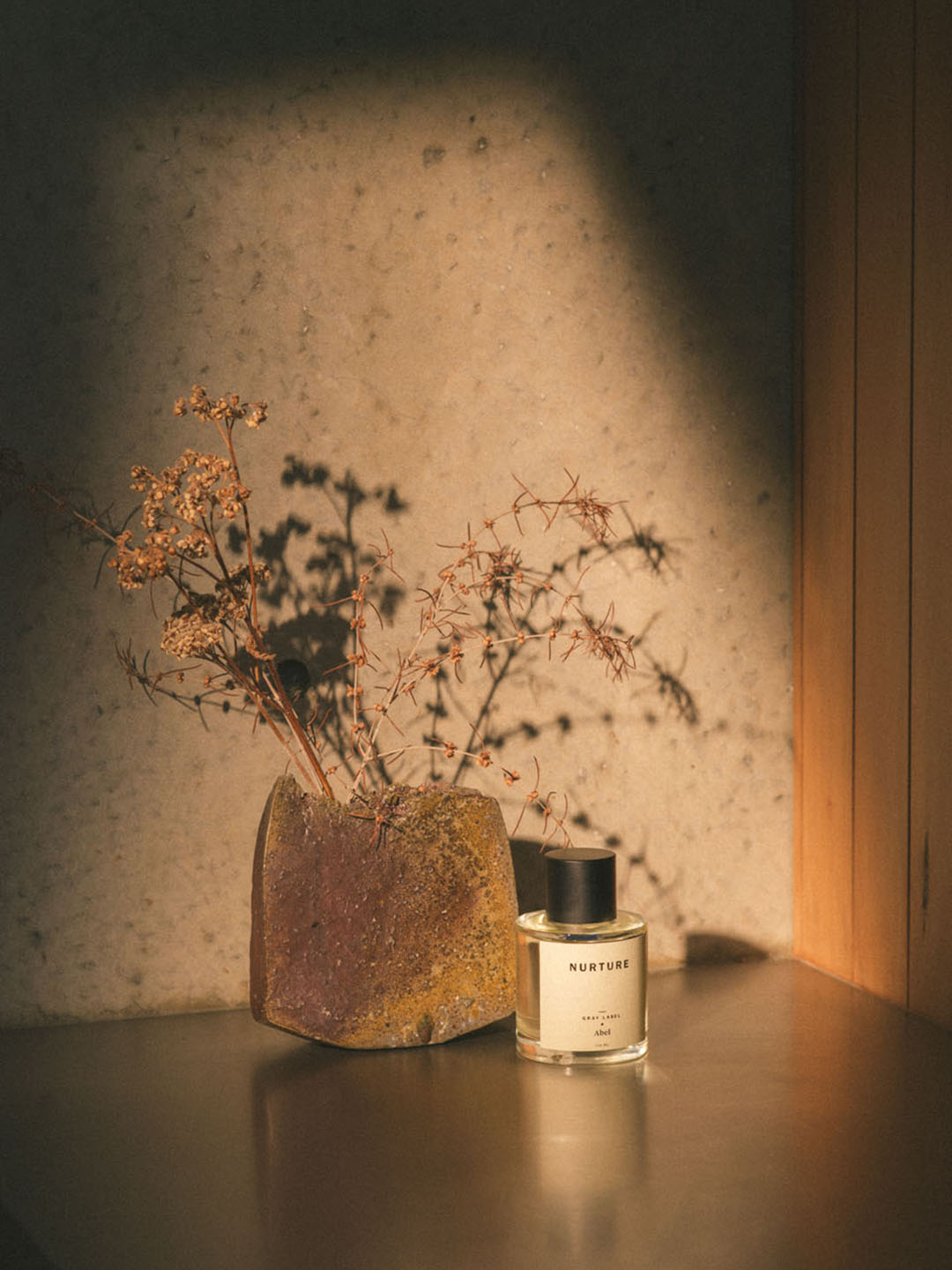 An NURTURE - grey label fragrance bottle sits on a table next to a plant by Abel.