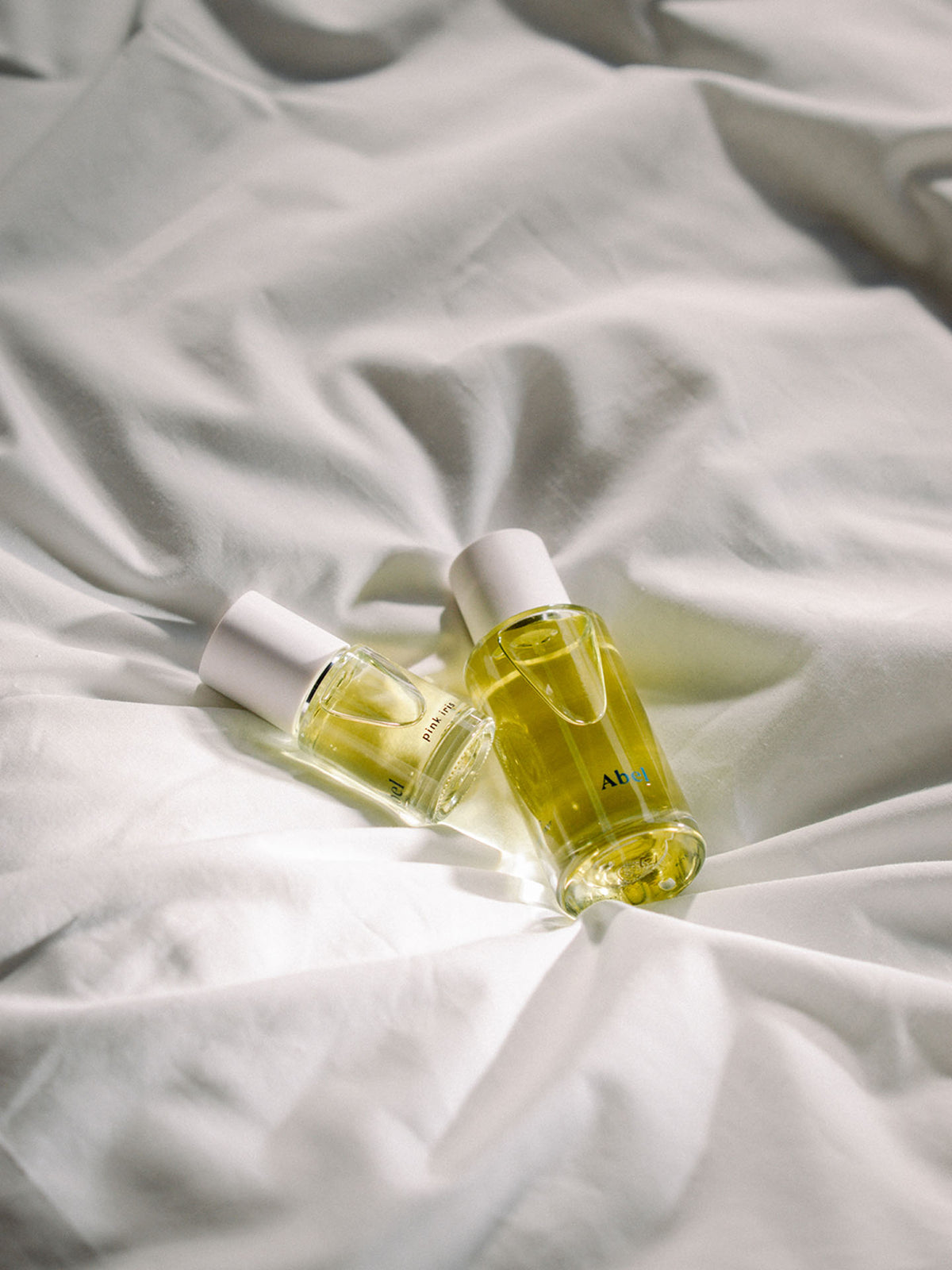 Two bottles of Abel&#39;s Pink Iris - a contemporary, classic floral perfume and Natural Musk perfume on a white bed.