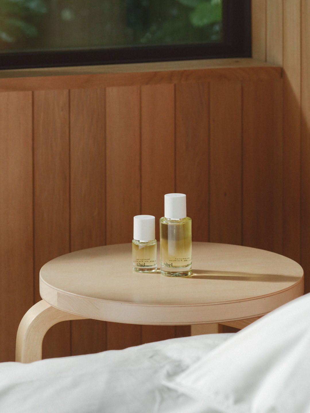 Two bottles of Abel's Pink Iris – a contemporary, classic floral essential oils, Sichuan pepper and iris, on a wooden table in a bedroom.