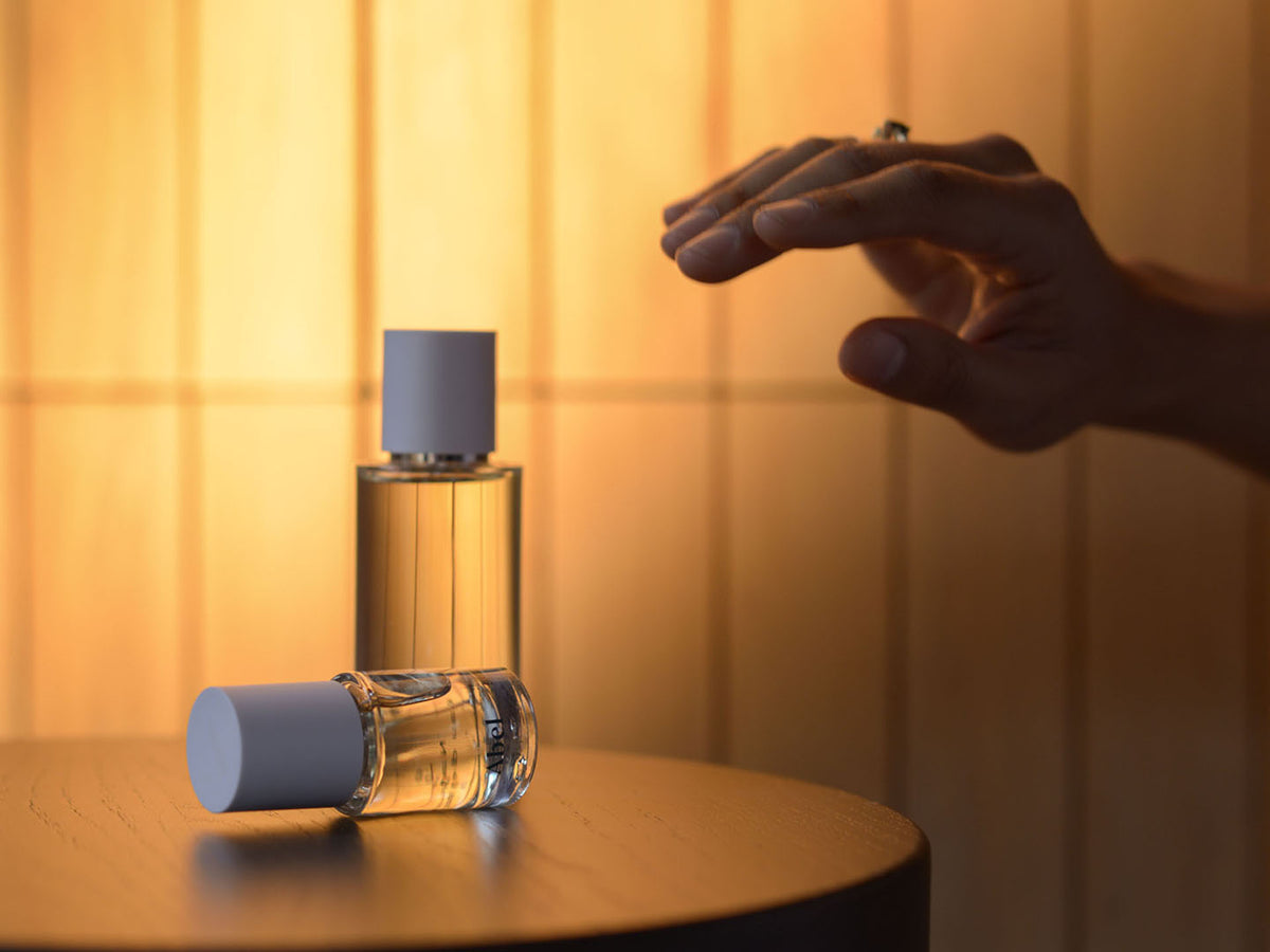 A hand reaching out to a bottle of Abel&#39;s Golden Neroli vegan eau de parfum on a wooden surface with warm lighting.