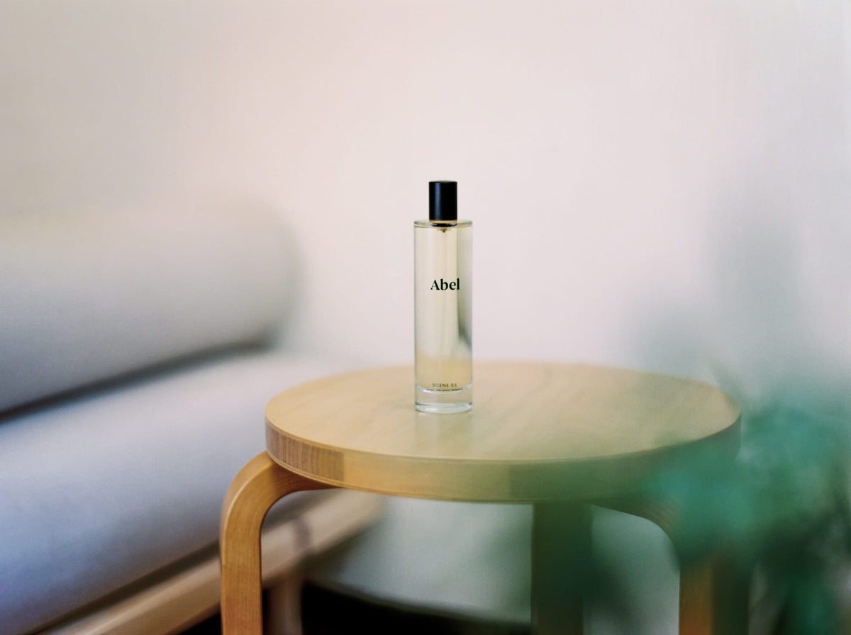 A bottle of Abel&#39;s Room Spray - Scene 01 ⋅ green tea, yuzu, verbena placed on a wooden round table in a softly lit room.