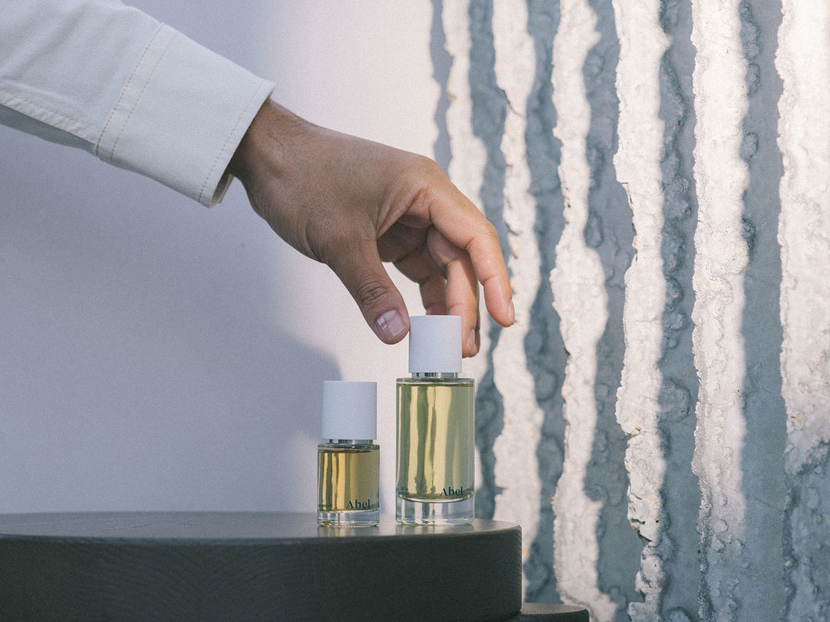 A hand reaching for a bottle of White Vetiver eau de parfum with Haitian vetiver on a shelf by Abel.
