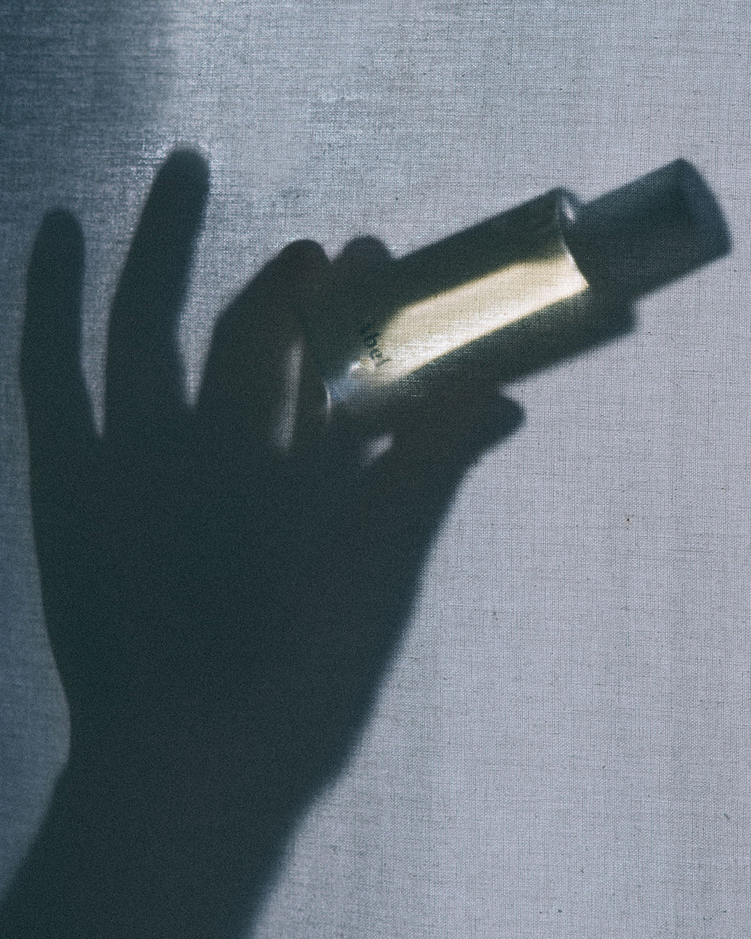 A natural shadow of a hand holding a Cobalt Amber perfume bottle with an Abel brand amber hue.