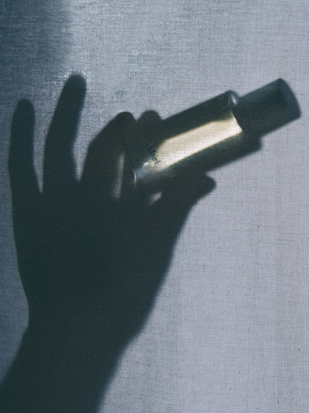 A natural shadow of a hand holding a Cobalt Amber perfume bottle with an Abel brand amber hue.
