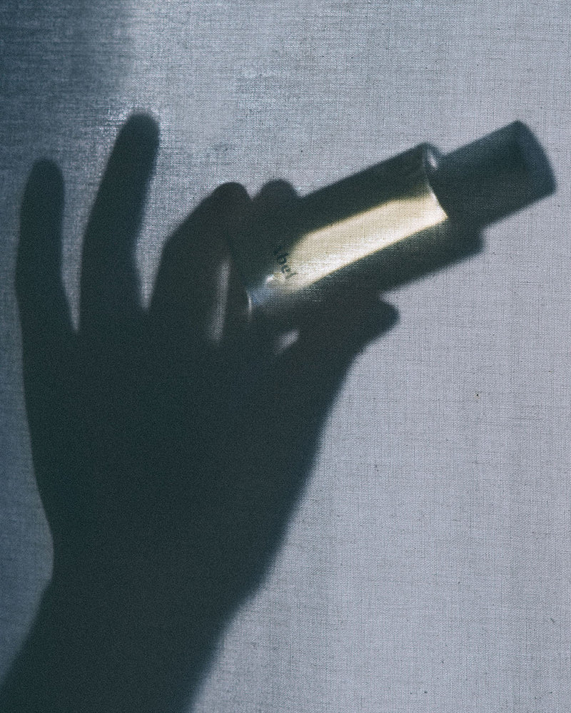 A natural shadow of a hand holding a Cobalt Amber perfume bottle with an Abel brand amber hue.
