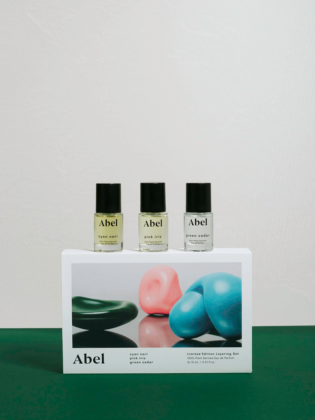 Three bottles of Abel Layering Set – Cyan Nori ⋄ Green Cedar ⋄ Pink Iris natural eau de parfum displayed in front of their packaging, which features images of colored stones.