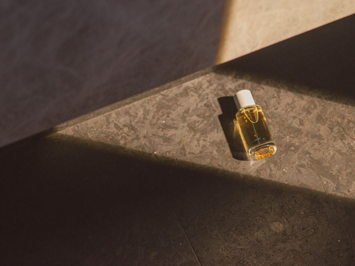 A bottle of Black Anise by Abel, a vibrant essential oil sitting on a stone floor, with hints of smoky amber and dynamic star anise.